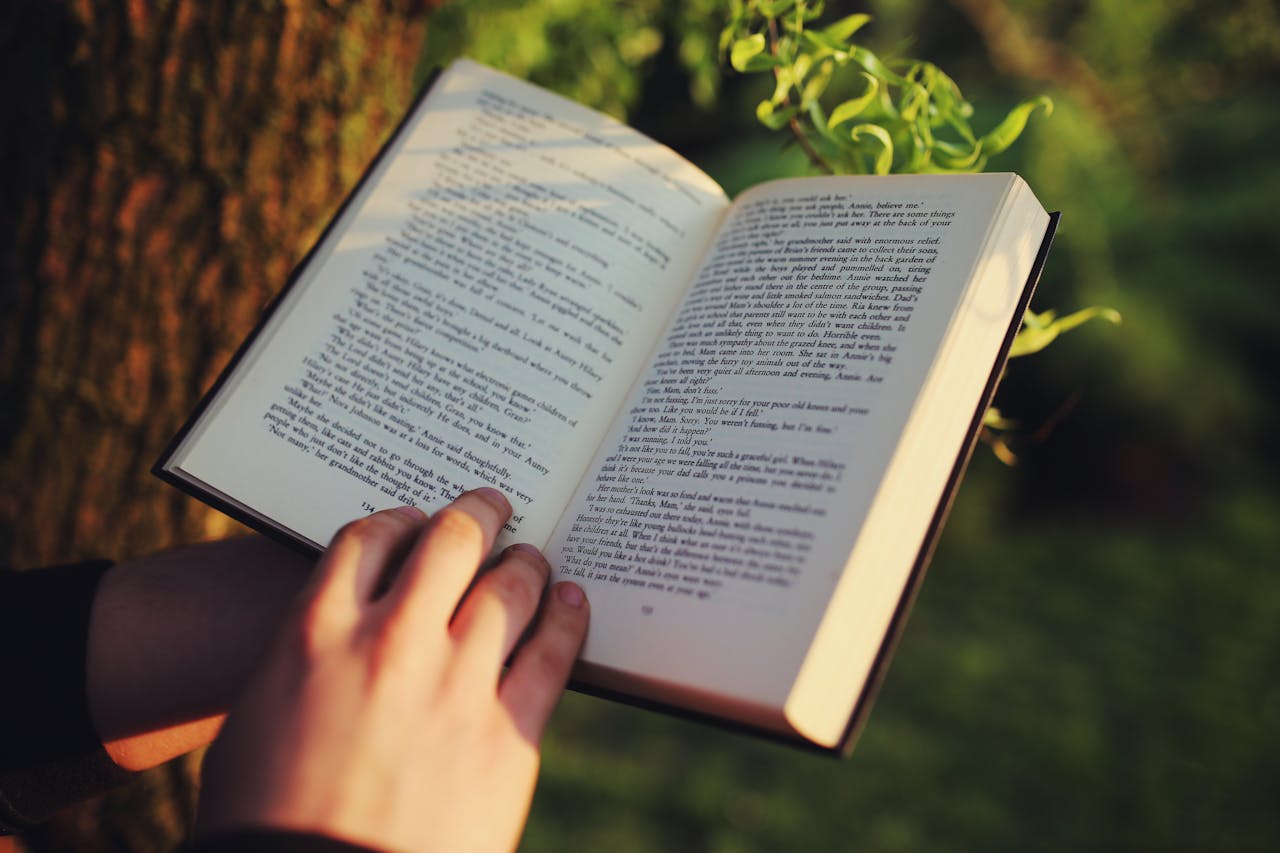 A person reading a book outdoors in a serene natural setting, immersed in literature.