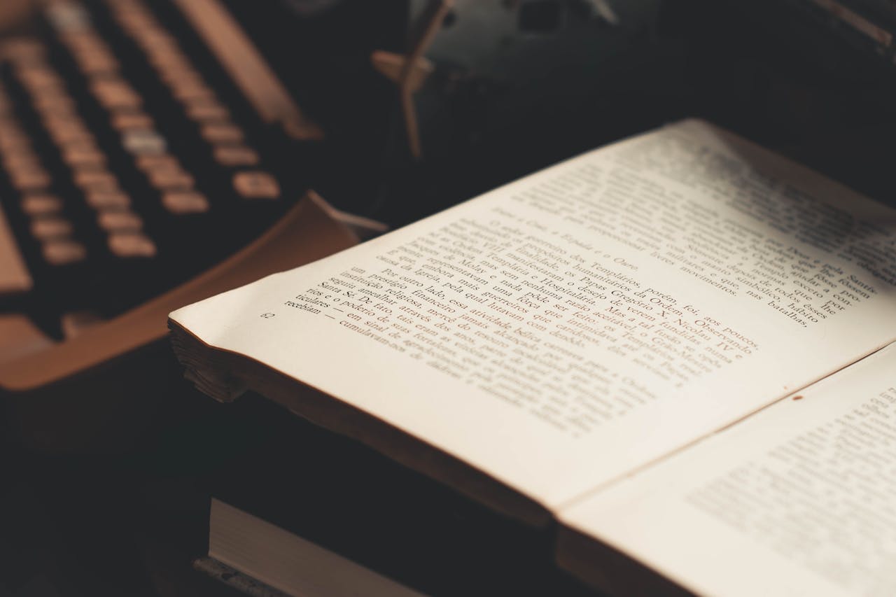 Home An open book with visible text in front of an antique typewriter, evoking a vintage literary theme.